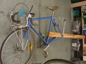 Using a 2x4 to spread the bike's rear triangle. (Do not attempt with anything but a steel frame bike)